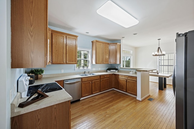 kitchen featuring light countertops, appliances with stainless steel finishes, a peninsula, light wood-style floors, and a sink