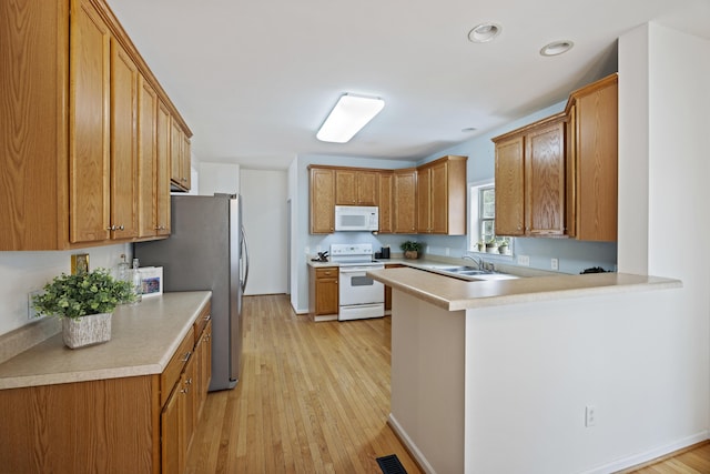 kitchen with light wood-type flooring, white appliances, a peninsula, and light countertops