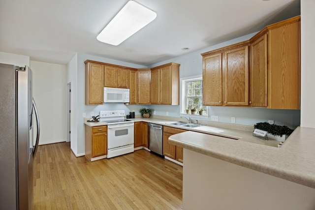 kitchen with a peninsula, a sink, stainless steel appliances, light countertops, and light wood-style floors