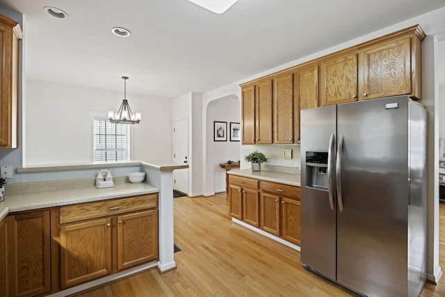 kitchen with brown cabinets, a peninsula, light wood-style flooring, stainless steel refrigerator with ice dispenser, and arched walkways