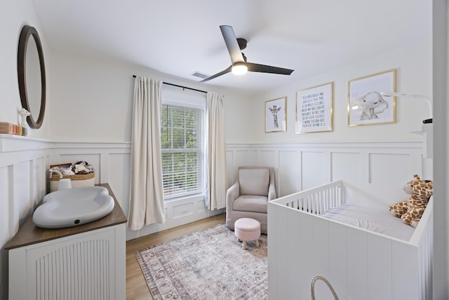 bedroom with visible vents, a crib, wood finished floors, a decorative wall, and a ceiling fan