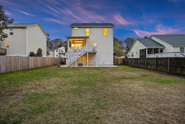 back of property at dusk with a fenced backyard, a patio, stairs, and a yard