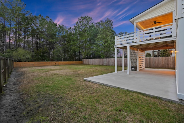 yard at dusk featuring a ceiling fan, a fenced backyard, stairway, a wooden deck, and a patio area