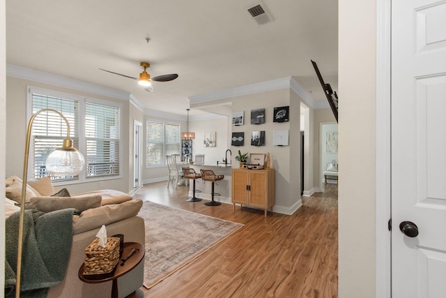 living room with a ceiling fan, visible vents, crown molding, and light wood finished floors