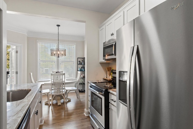 kitchen with dark wood-style floors, appliances with stainless steel finishes, ornamental molding, white cabinetry, and a notable chandelier