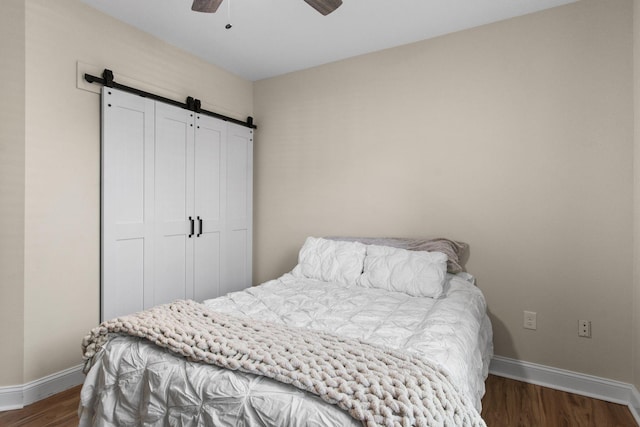 bedroom featuring a barn door, wood finished floors, a ceiling fan, and baseboards