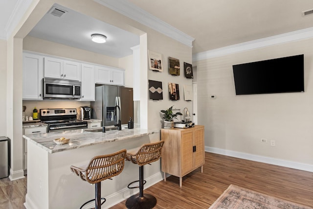 kitchen with light stone counters, a breakfast bar, white cabinetry, light wood-style floors, and appliances with stainless steel finishes