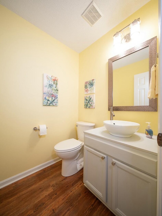 half bathroom featuring visible vents, toilet, vanity, wood finished floors, and a textured ceiling