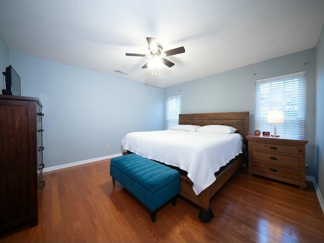 bedroom featuring a ceiling fan, wood finished floors, visible vents, and baseboards