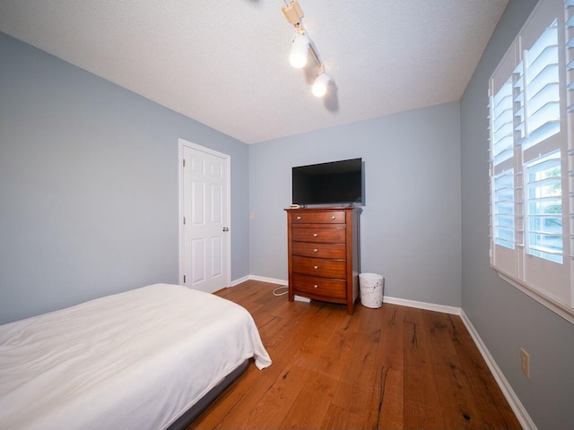 bedroom with baseboards, a textured ceiling, and wood finished floors