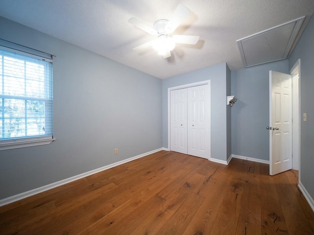 unfurnished bedroom featuring a ceiling fan, hardwood / wood-style flooring, a closet, baseboards, and attic access