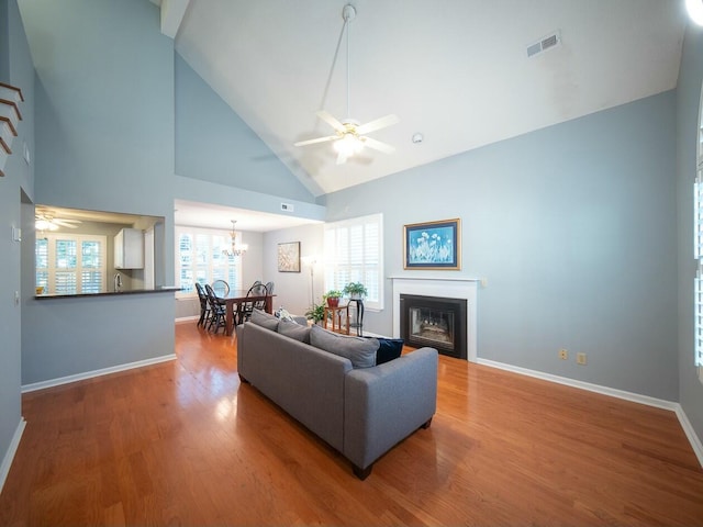 living room with visible vents, ceiling fan with notable chandelier, wood finished floors, a glass covered fireplace, and baseboards