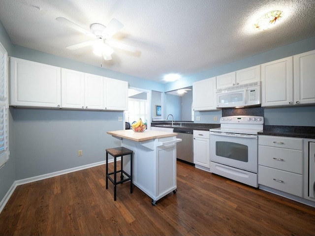 kitchen with a sink, a kitchen bar, white appliances, white cabinetry, and dark wood-style flooring