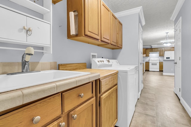 clothes washing area with cabinets, sink, crown molding, washing machine and dryer, and a textured ceiling