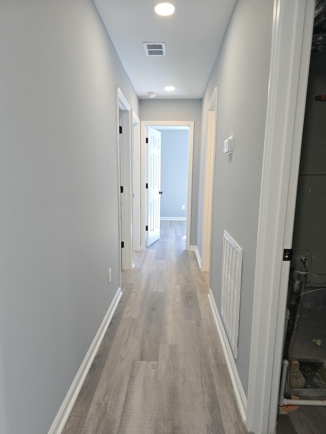 hallway featuring baseboards, visible vents, and light wood finished floors