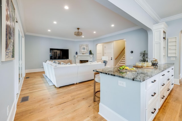 kitchen with a kitchen bar, light wood-style flooring, ornamental molding, arched walkways, and white cabinets