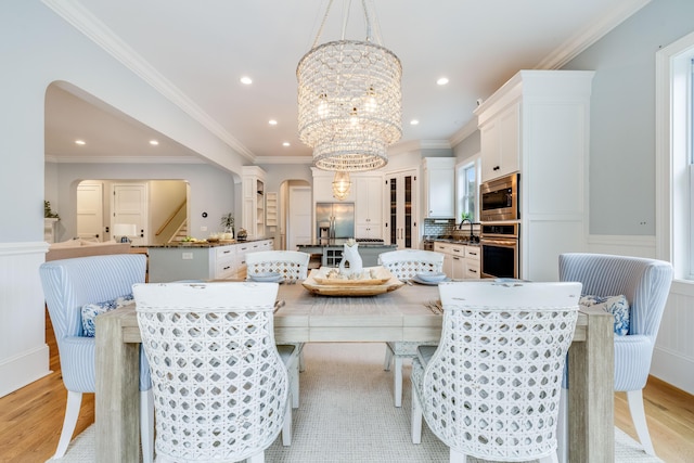 dining space featuring a wainscoted wall, a notable chandelier, arched walkways, and light wood-type flooring