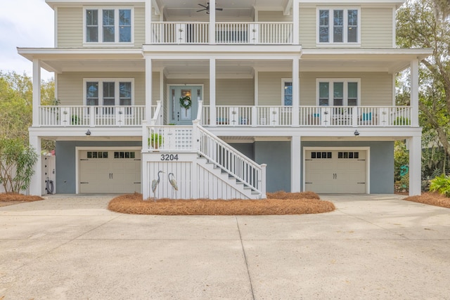 raised beach house with a porch, stairway, concrete driveway, and a garage