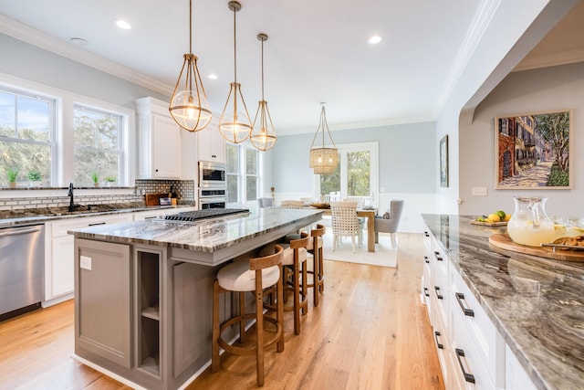 kitchen with a kitchen island, light wood-style flooring, ornamental molding, a sink, and appliances with stainless steel finishes