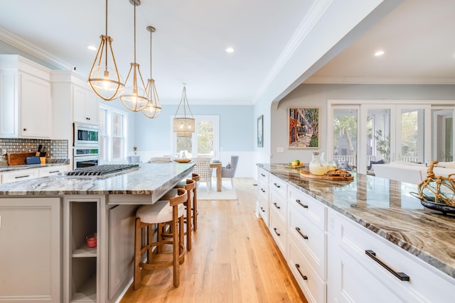 kitchen with light wood-type flooring, ornamental molding, a kitchen breakfast bar, white cabinetry, and appliances with stainless steel finishes