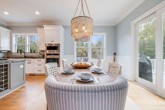 dining room featuring light wood-type flooring, ornamental molding, recessed lighting, wainscoting, and a chandelier