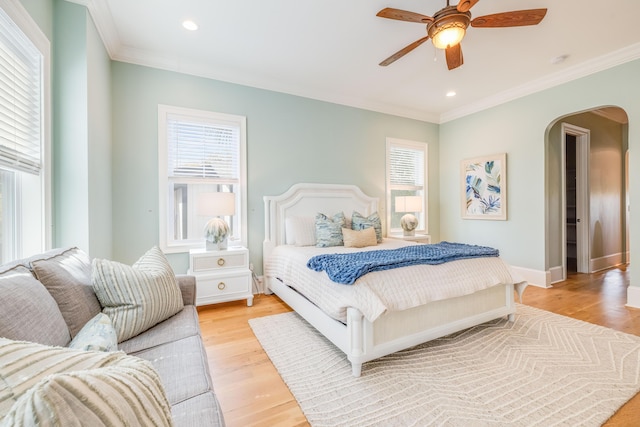 bedroom with arched walkways, multiple windows, light wood-style flooring, and crown molding