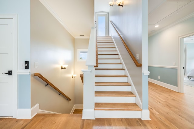 stairs with baseboards, wood finished floors, and crown molding