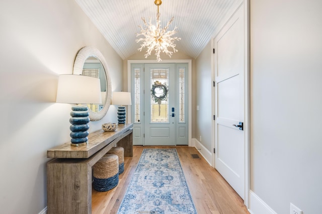 foyer entrance with an inviting chandelier, light wood-style floors, baseboards, and vaulted ceiling