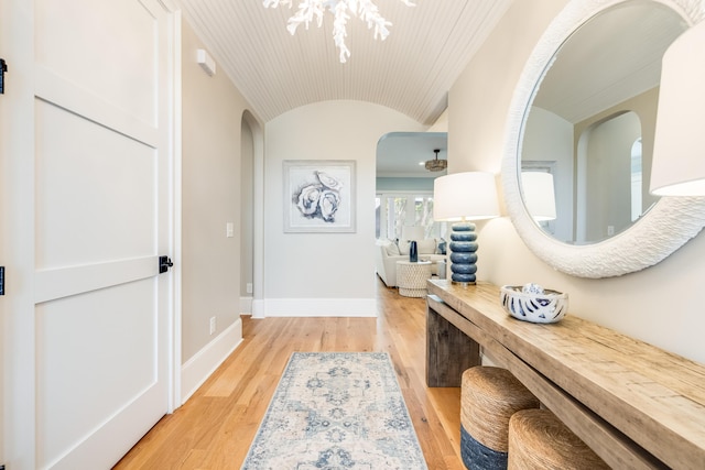 hallway with light wood-type flooring, baseboards, arched walkways, and vaulted ceiling