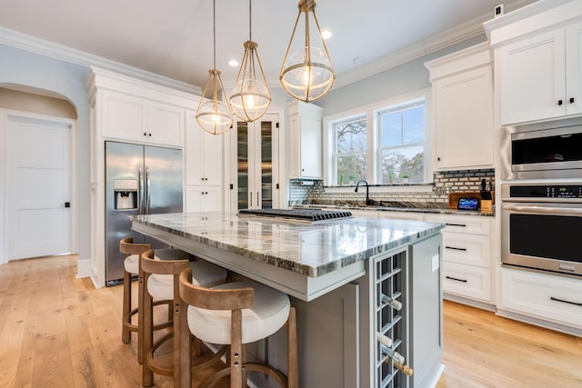 kitchen featuring a kitchen island, crown molding, light stone counters, decorative backsplash, and appliances with stainless steel finishes