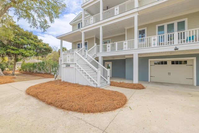 coastal inspired home with a porch, an attached garage, concrete driveway, and stairs