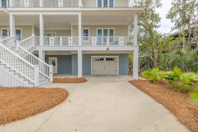 coastal inspired home featuring stairs, a porch, an attached garage, and driveway