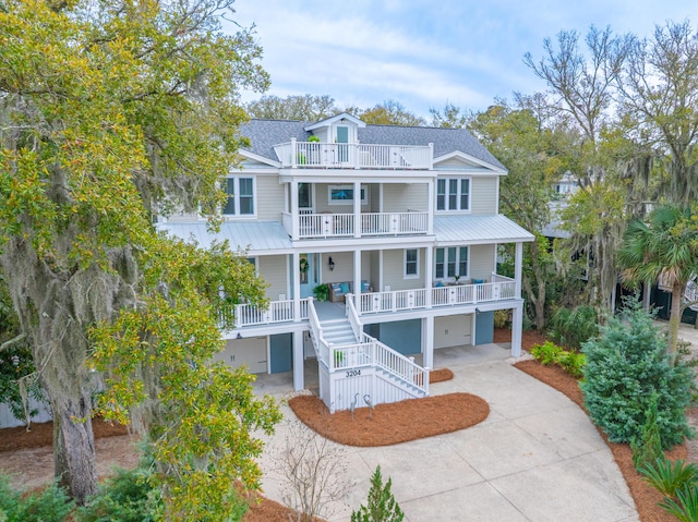 coastal inspired home featuring a porch, concrete driveway, stairs, a balcony, and an attached garage