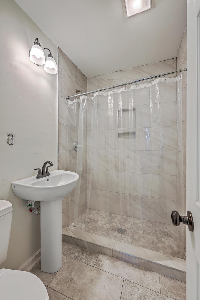 bathroom with baseboards, a tile shower, and toilet