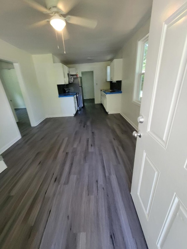 unfurnished living room featuring dark wood-type flooring, baseboards, and a ceiling fan