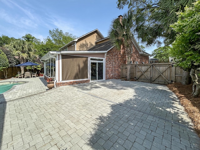 back of house with a chimney, a gate, brick siding, fence, and a patio