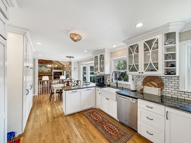 kitchen featuring stainless steel dishwasher, dark countertops, a sink, a peninsula, and crown molding
