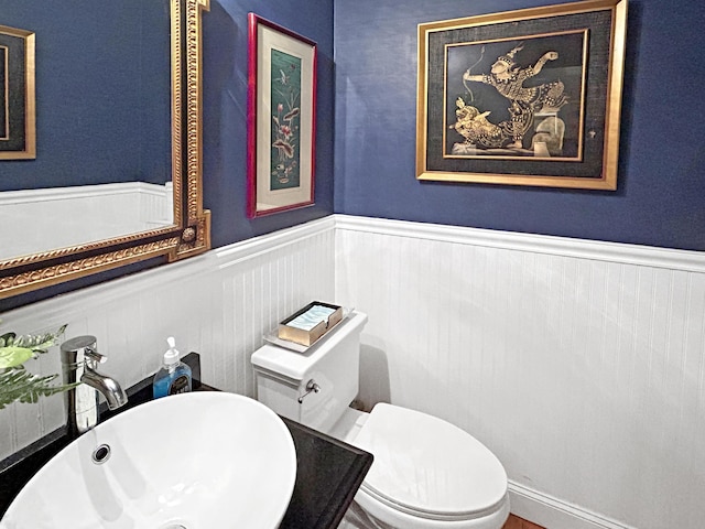 bathroom with toilet, a wainscoted wall, and a sink