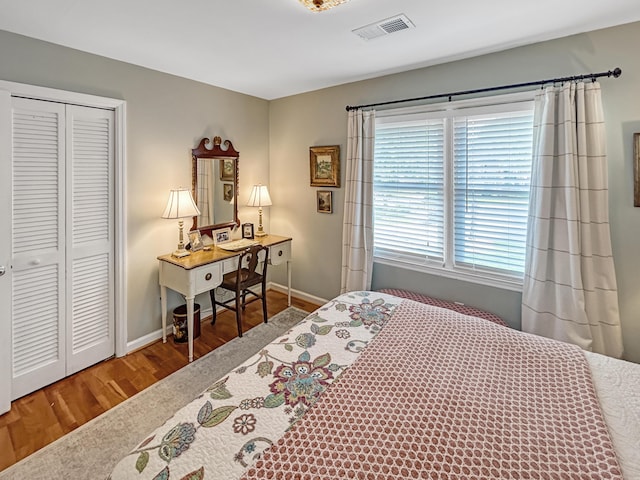 bedroom with baseboards, visible vents, wood finished floors, and a closet