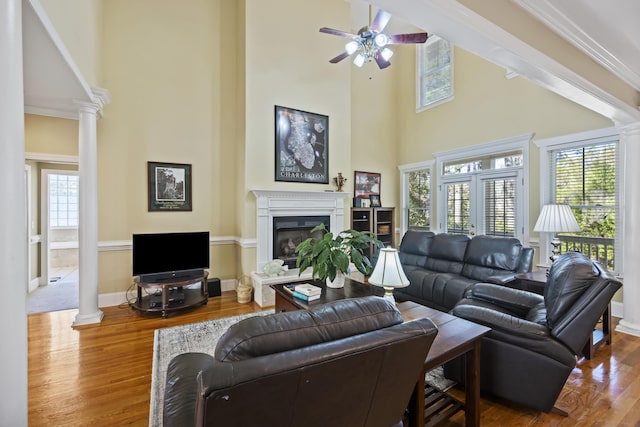 living room with hardwood / wood-style flooring, ceiling fan, ornate columns, and a towering ceiling