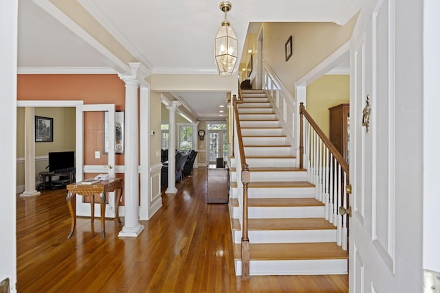 foyer entrance with decorative columns, dark wood-type flooring, a chandelier, and ornamental molding