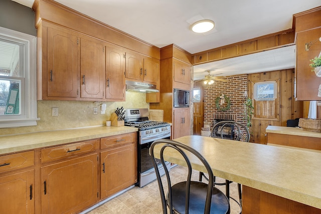 kitchen featuring a brick fireplace, stainless steel gas range, ceiling fan, black microwave, and brick wall