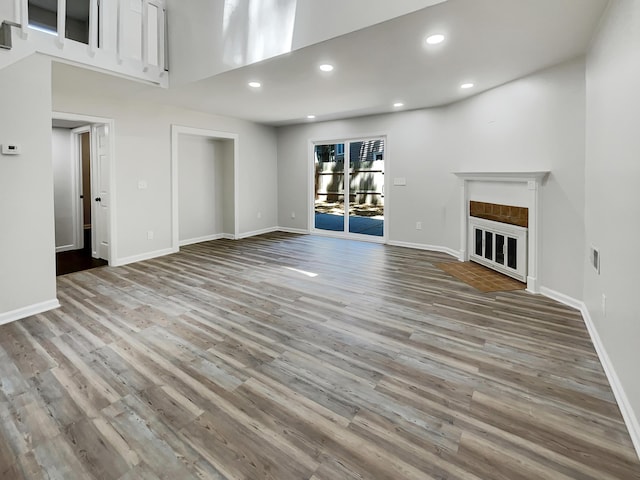 unfurnished living room with a glass covered fireplace, baseboards, recessed lighting, and wood finished floors