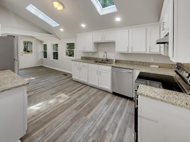 kitchen with stainless steel appliances, sink, vaulted ceiling with skylight, and white cabinets