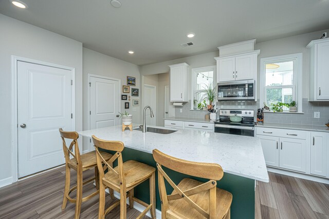 kitchen featuring white cabinets, appliances with stainless steel finishes, light stone countertops, sink, and a center island with sink