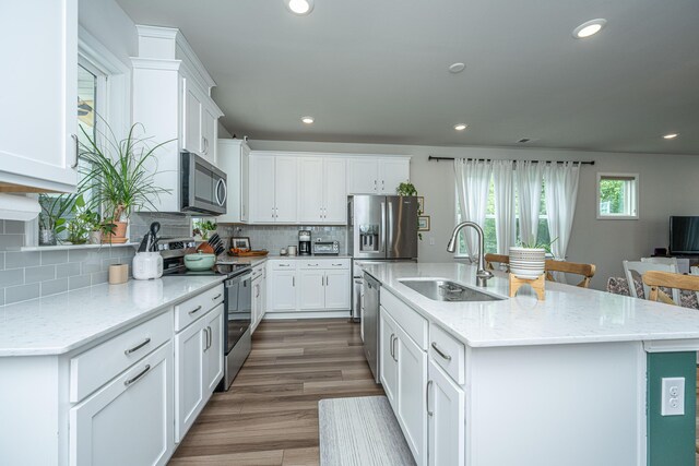 kitchen featuring hardwood / wood-style floors, stainless steel appliances, sink, light stone countertops, and a center island with sink