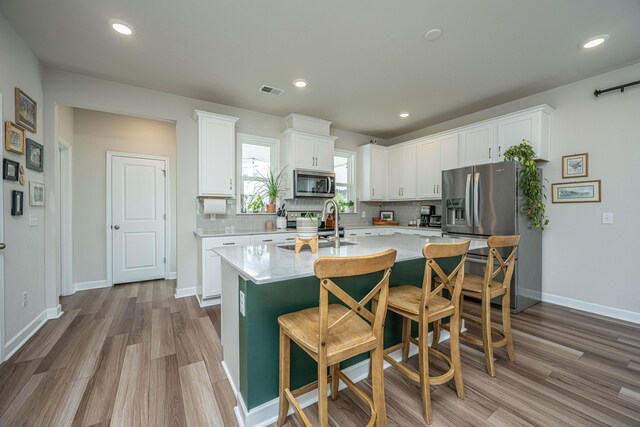 kitchen featuring a kitchen breakfast bar, hardwood / wood-style floors, appliances with stainless steel finishes, a kitchen island with sink, and white cabinetry