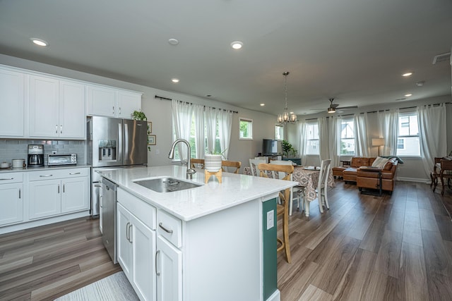 kitchen with a sink, wood finished floors, open floor plan, appliances with stainless steel finishes, and decorative backsplash