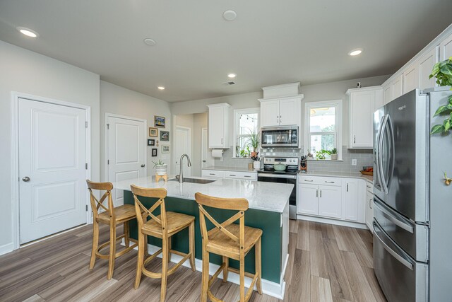 kitchen featuring a kitchen island with sink, stainless steel appliances, sink, white cabinets, and light hardwood / wood-style floors