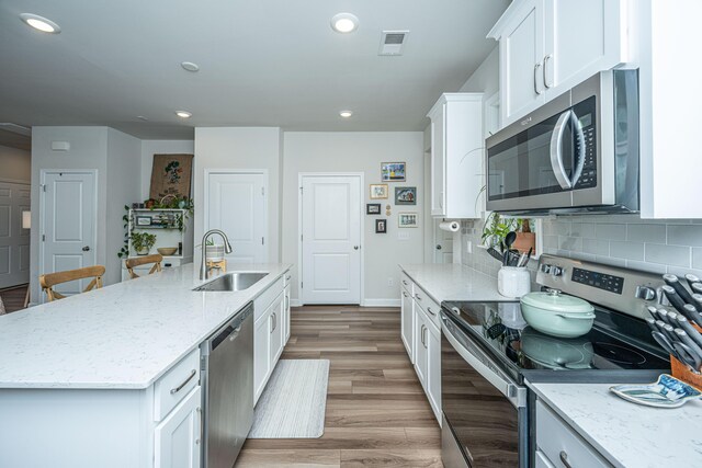 kitchen with light hardwood / wood-style flooring, stainless steel appliances, an island with sink, sink, and white cabinets